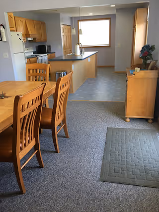 Open-plan dining area with a wooden table and chairs leading to a kitchen with an island, sink, and appliances.