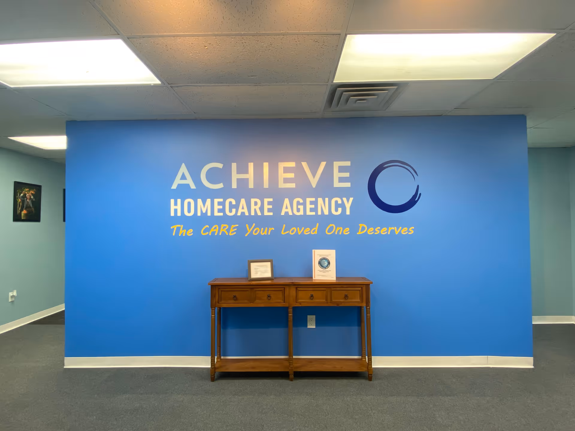 Blue interior wall with ACHIEVE Homecare Agency sign and a wooden console table.