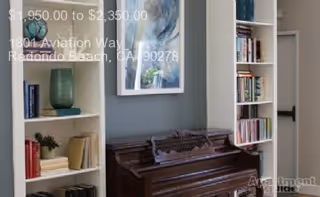 Interior room with an upright piano between built-in bookshelves and framed artwork on a gray wall.