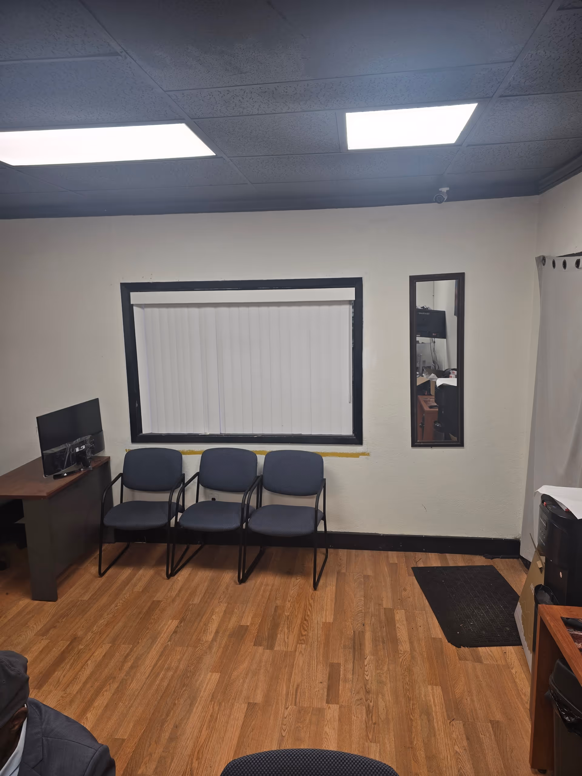 A small interior waiting area with four blue chairs, a desk, and a window.
