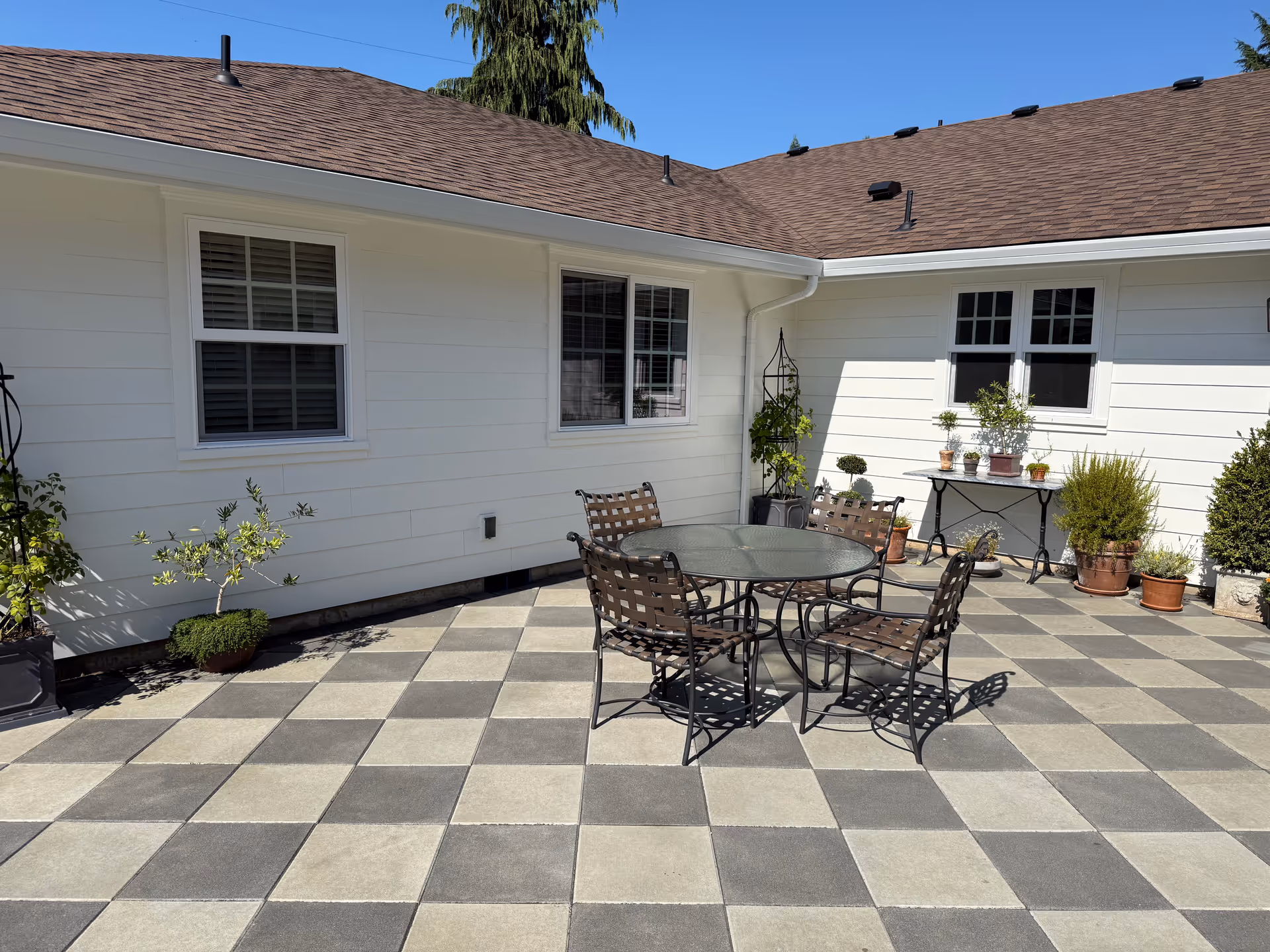 Checkerboard-tiled outdoor patio with a round glass table and metal chairs.