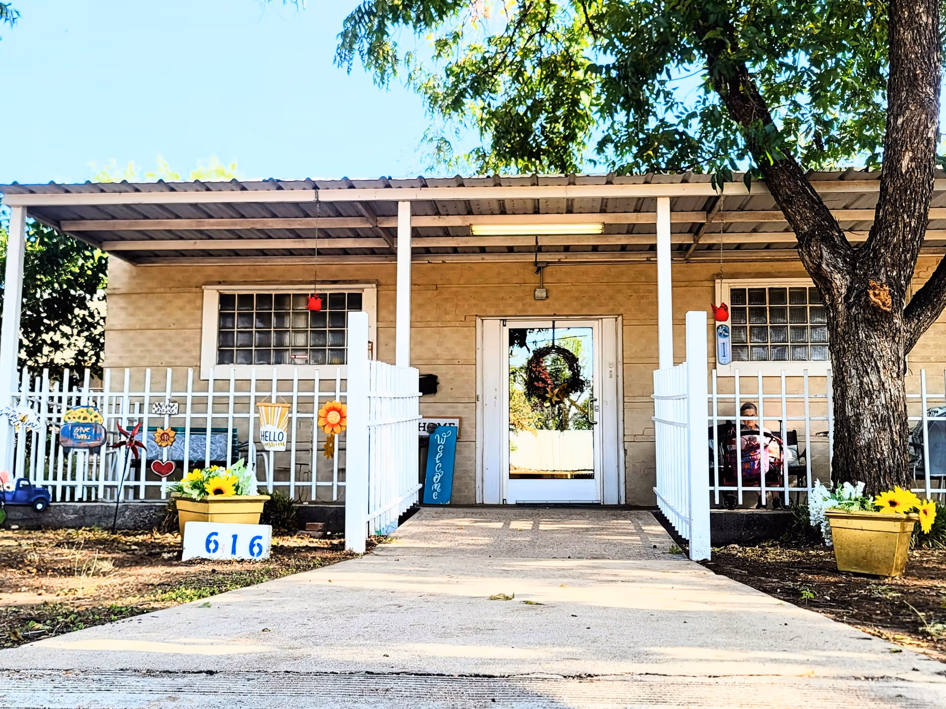 Front entrance of Winters Assisted Living Inc with a porch, wreath, white fence, and planters.
