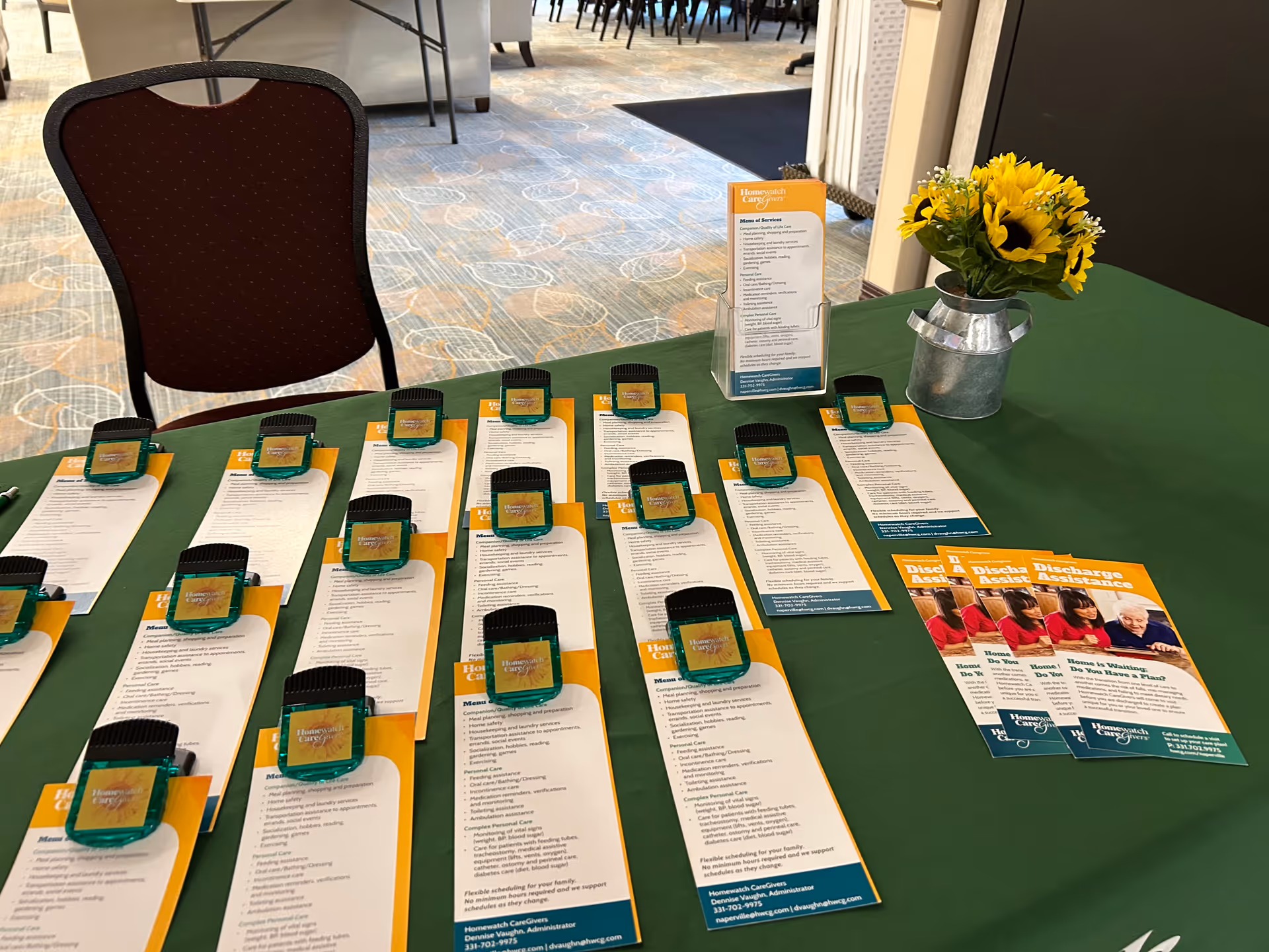 Promotional table with brochures, small devices, and a sunflower centerpiece inside a facility lobby