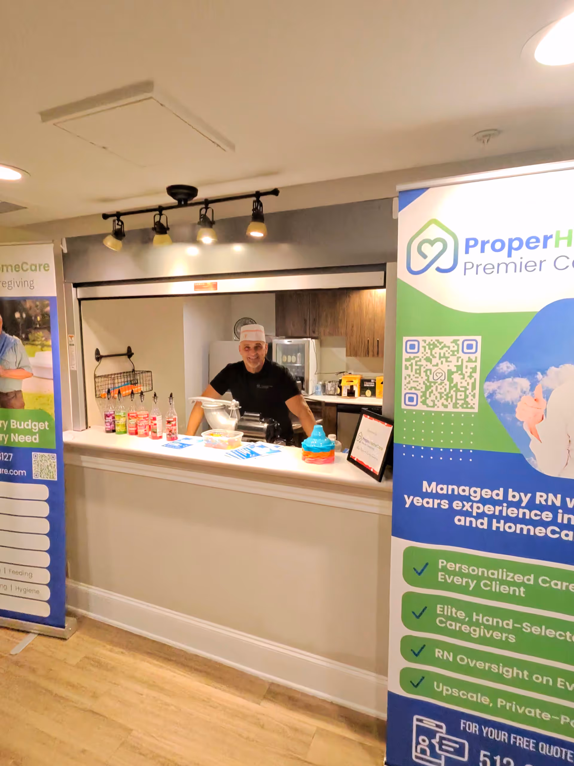Staff member at a service counter behind Proper Home Care banners inside a senior living facility.