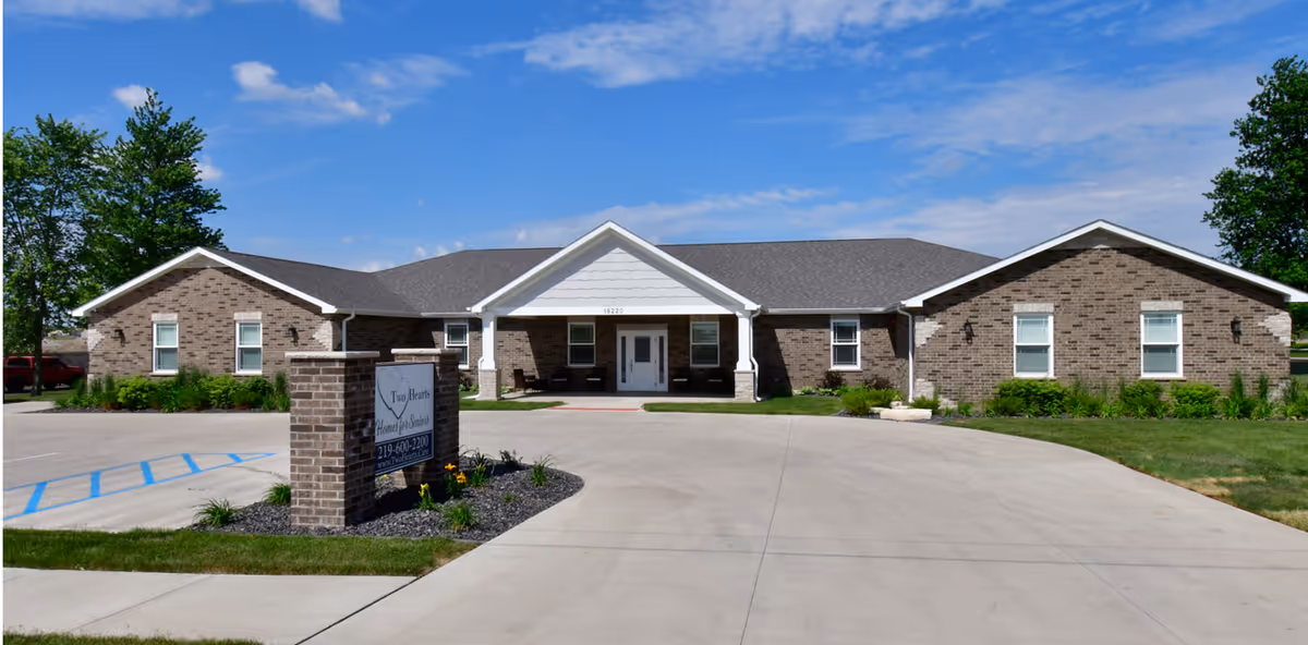 A single-story brick senior living facility exterior with a curved driveway and entry sign.