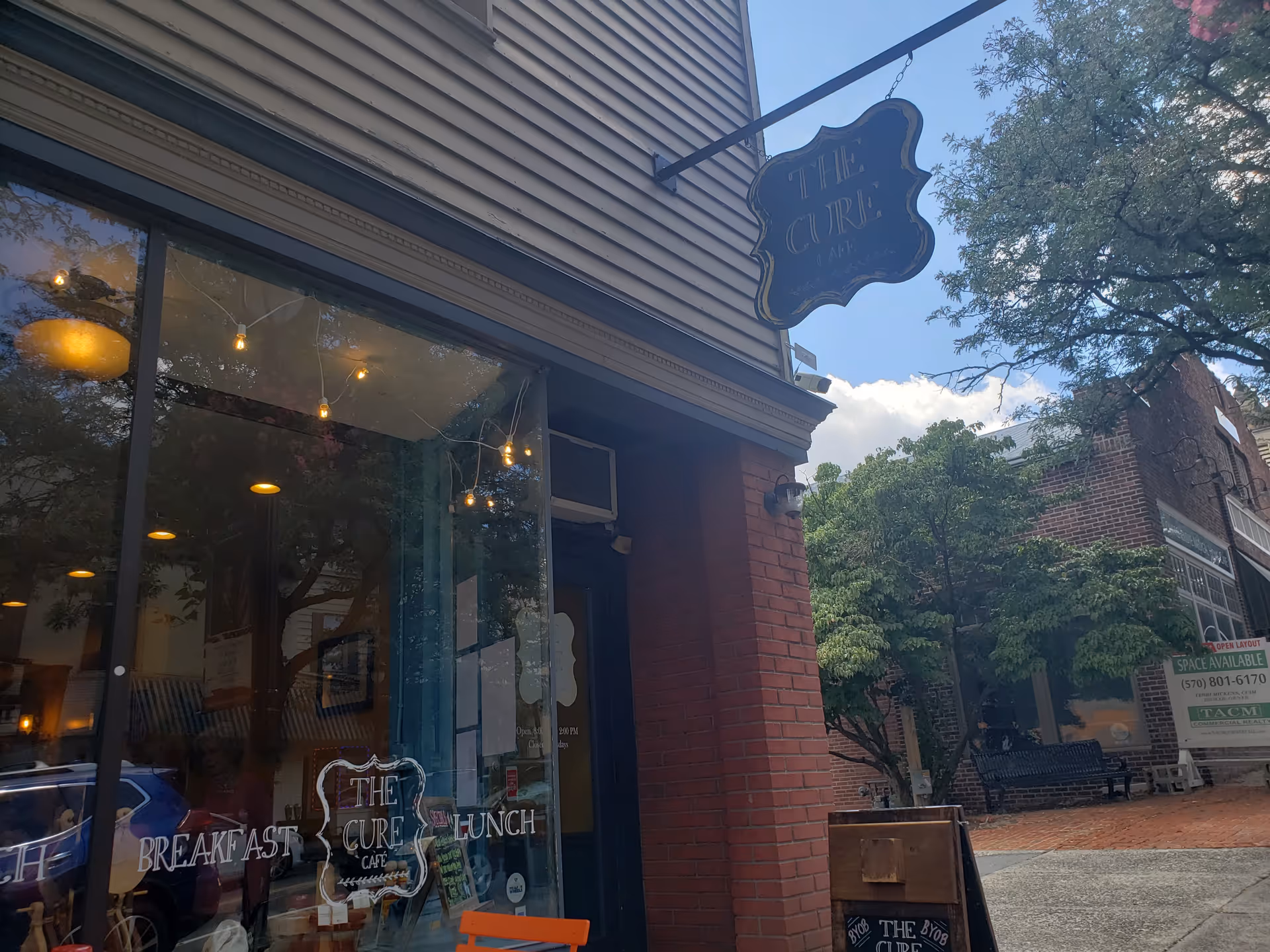 Exterior view of The Cure Café storefront with glass windows and hanging sign.