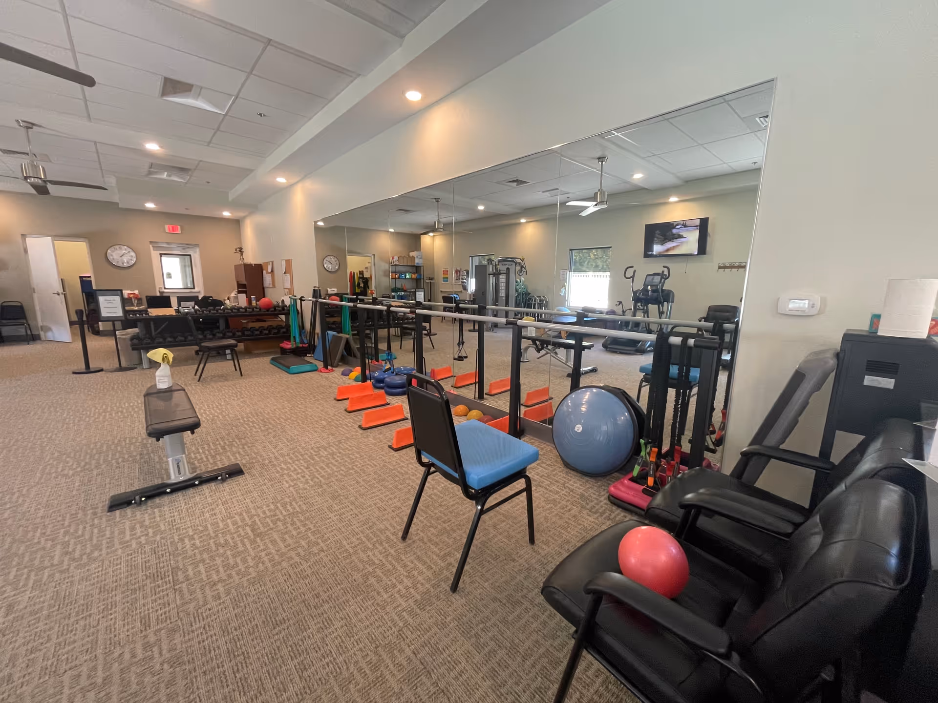Senior living fitness room with mirrors, yoga mats, exercise balls, weights, and seating.