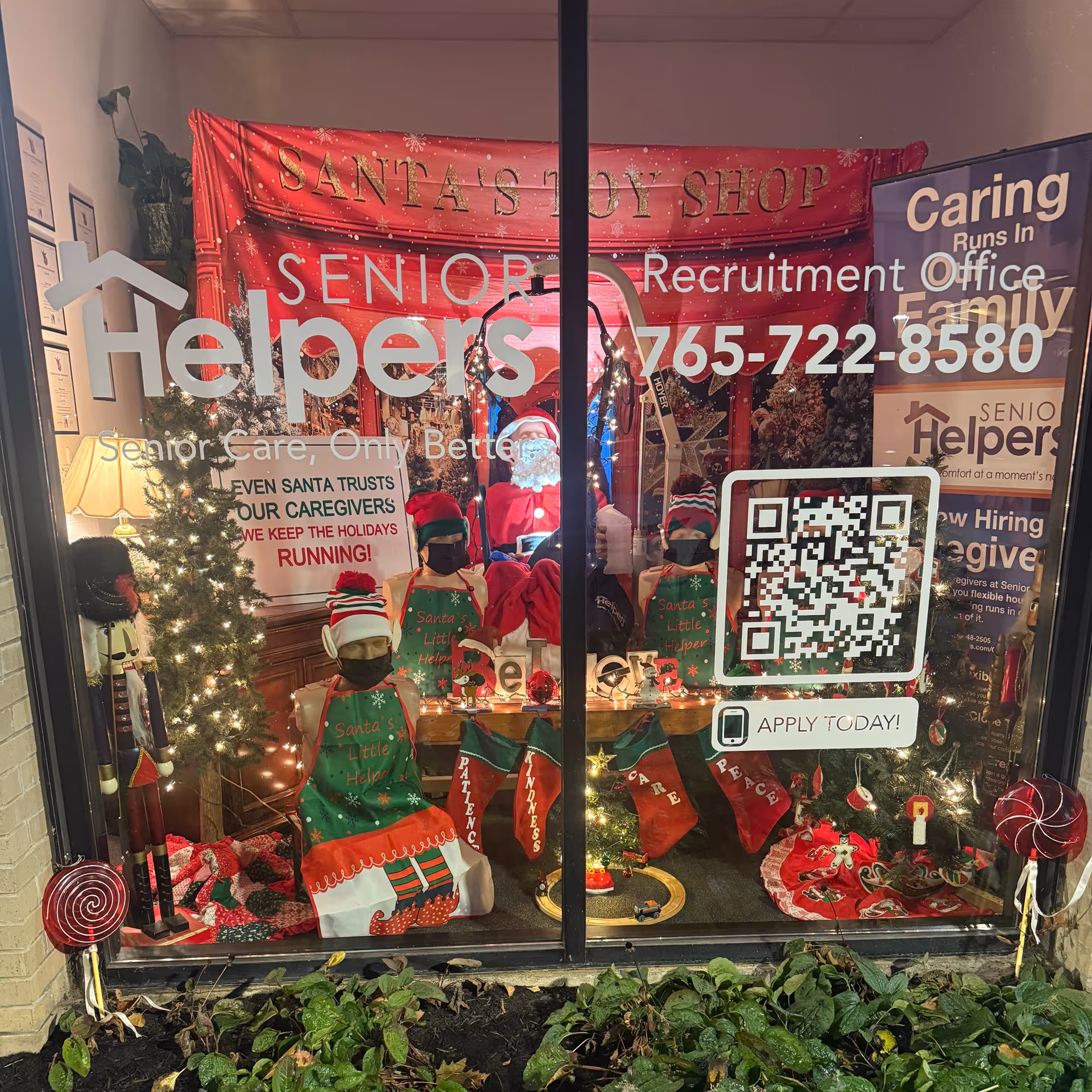 Glass storefront window decorated with Santa and elves, advertising Senior Helpers recruitment in East Central Indiana.