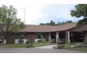 Single-story brick building with brown roof and front entrance canopy, landscaped grounds.