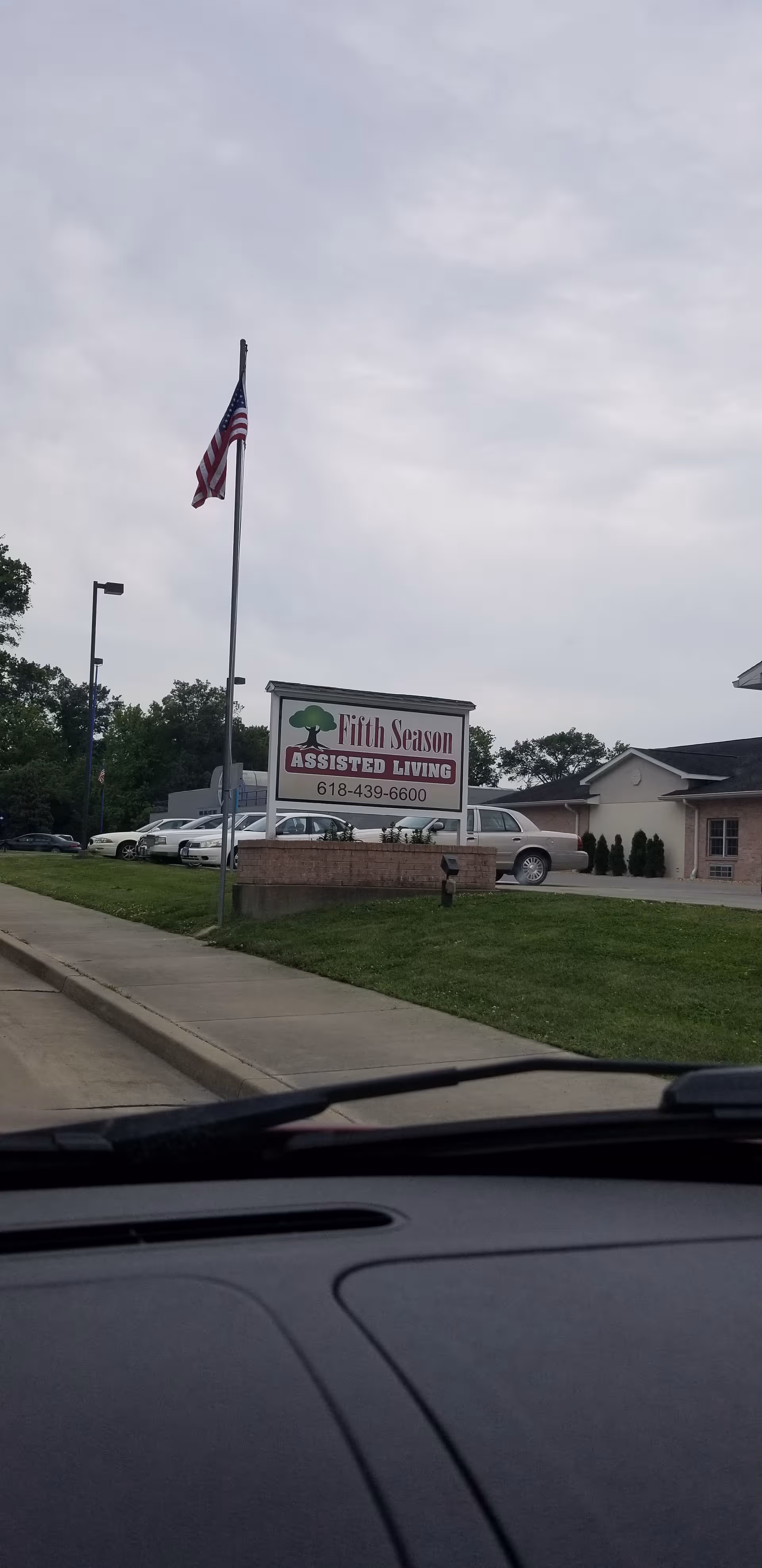 Front exterior of Fifth Season Assisted Living with sign, flagpole, and parked cars.