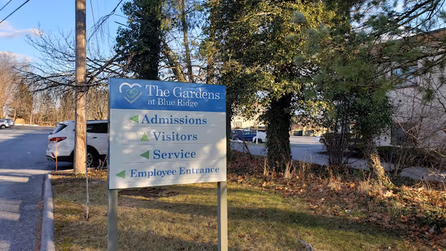Outdoor sign for The Gardens at Blue Ridge directing Admissions, Visitors, Service, and Employee Entrance near a parking area.