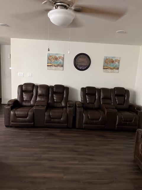 Interior living room with brown leather recliners, a ceiling fan, and wall art.