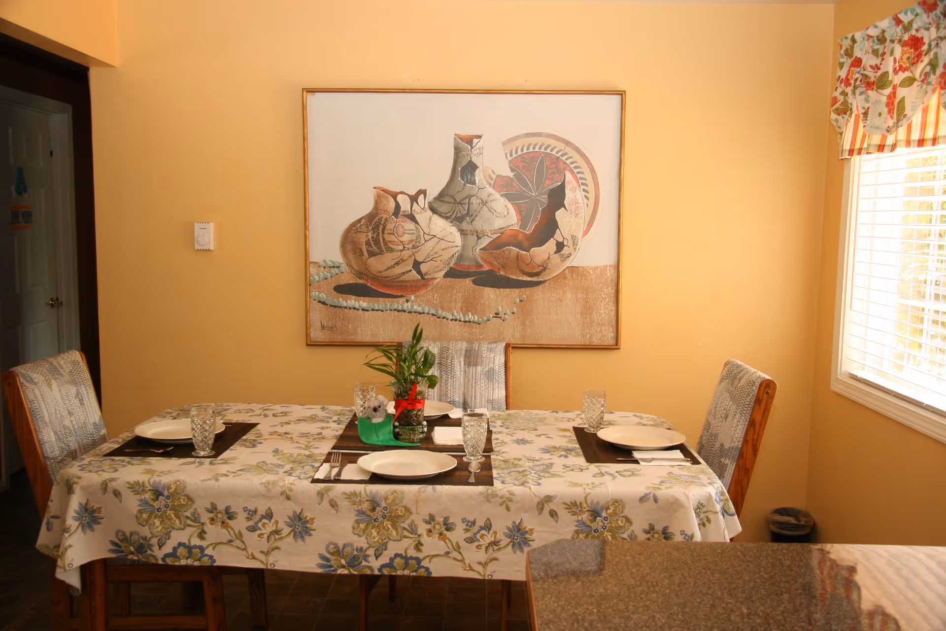 Dining room with a floral tablecloth, place settings, and wall art.