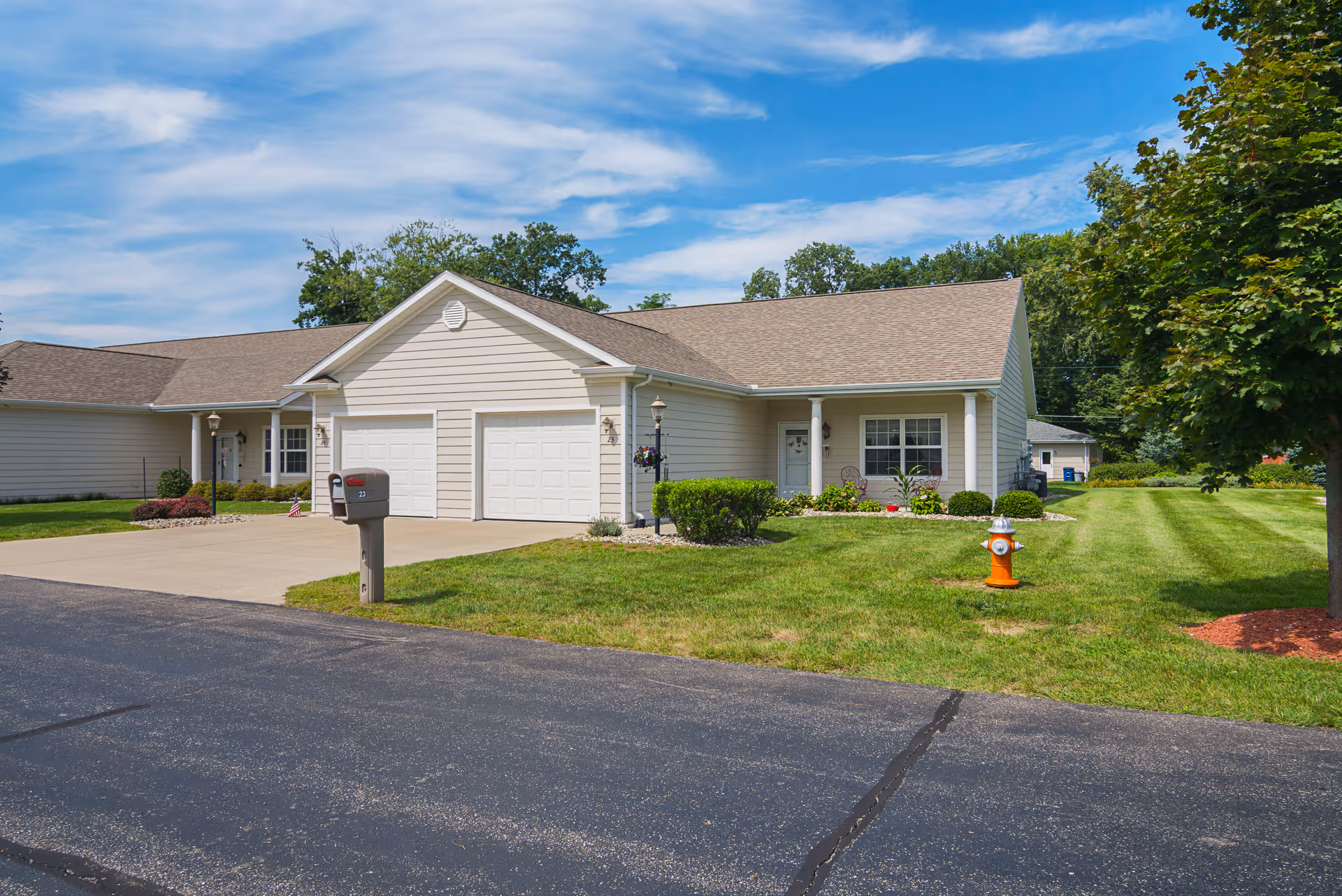 Single-story senior living facility with beige siding, a two-car garage, and green lawn.