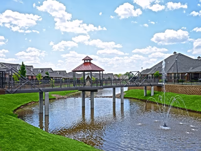 Outdoor view of a pedestrian bridge over a pond with fountains at Grace Pointe