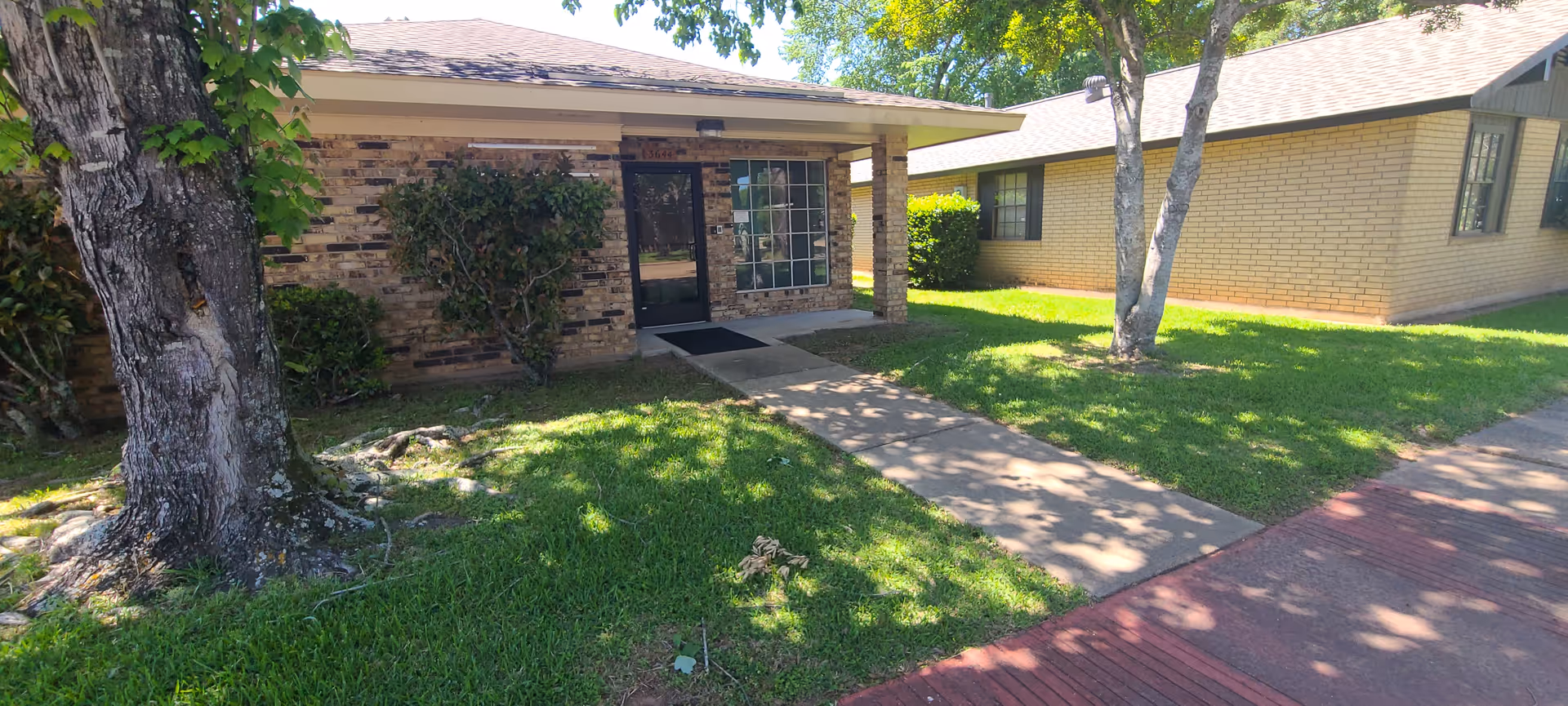Front exterior of a brick senior care facility with a walkway and trees.