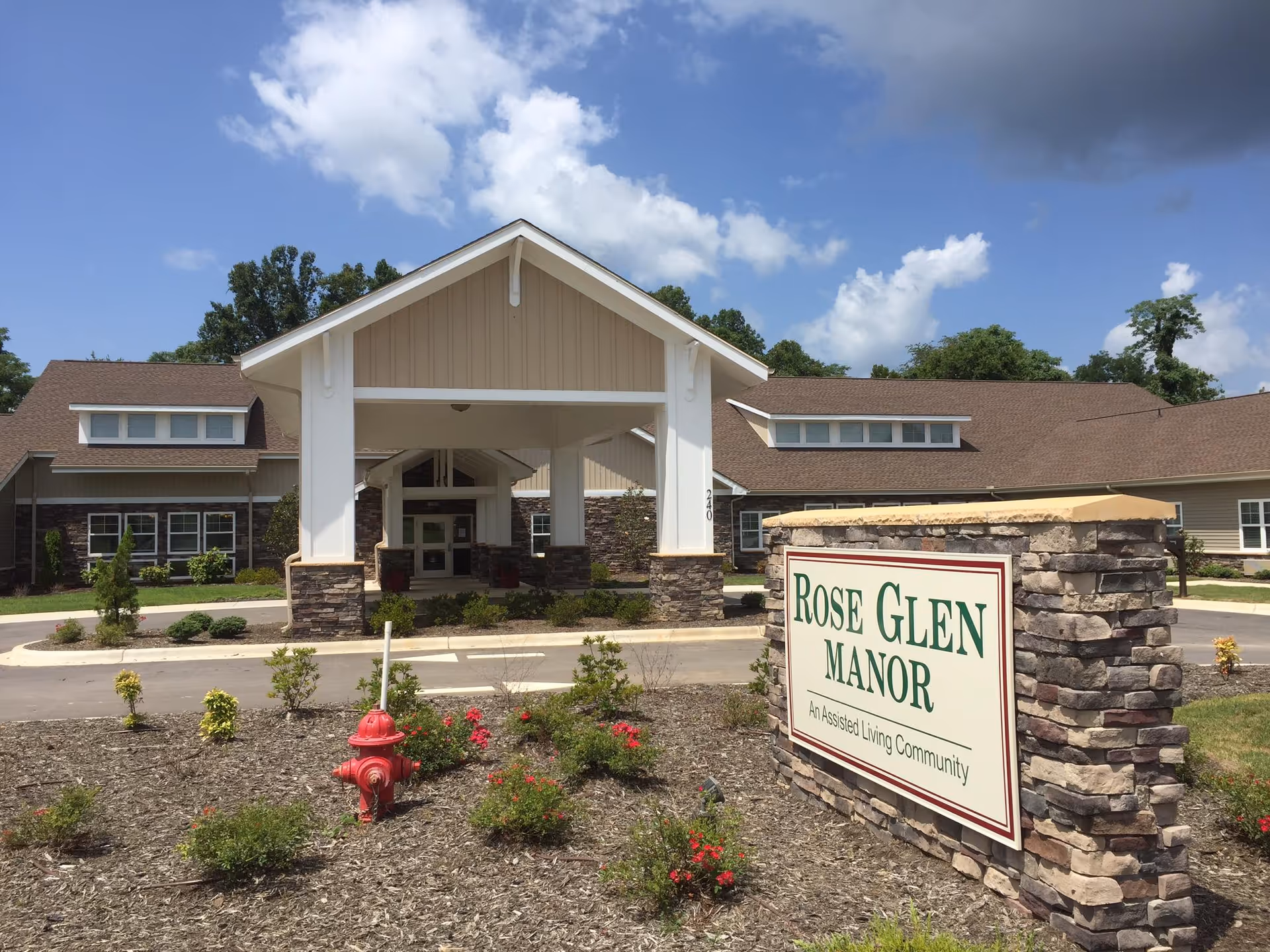 Entrance of Rose Glen Manor assisted living building with a covered porte-cochère, sign, and landscaped front.