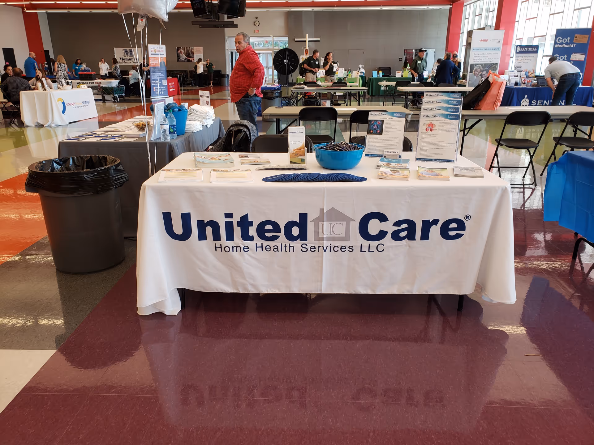 Indoor community health fair with booths, visitors, and a United Care Home Health Services table.