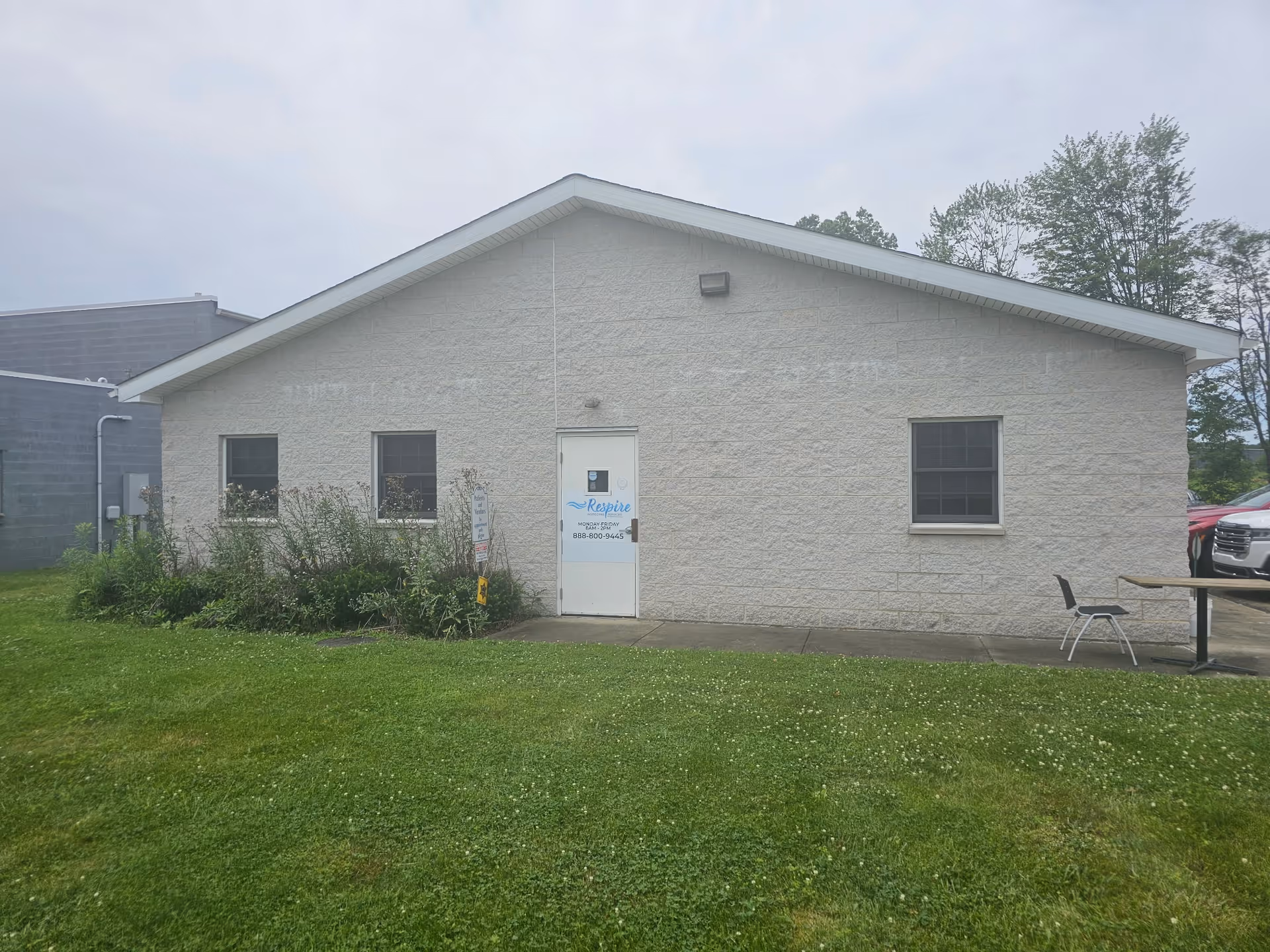 Front view of a single-story beige building with a door, window, and surrounding greenery.