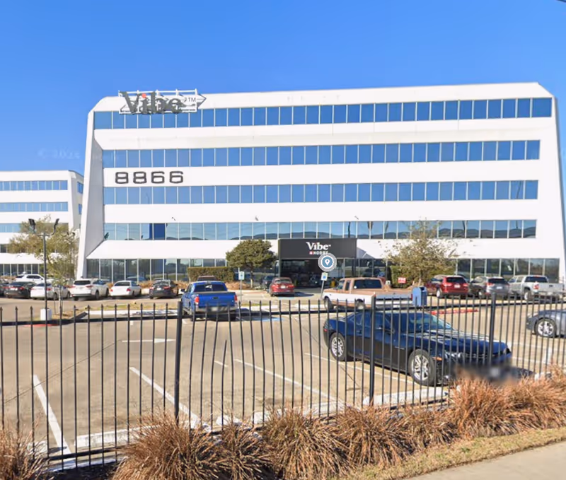 Front view of a white, multi-story building with blue windows and a parking lot.