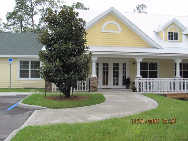 Yellow assisted living facility front entrance with curved walkway and tree.