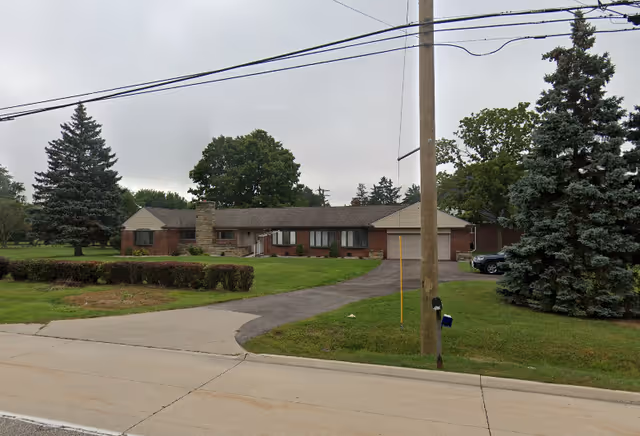 Single story brick senior housing building with lawn, trees, and curved driveway.
