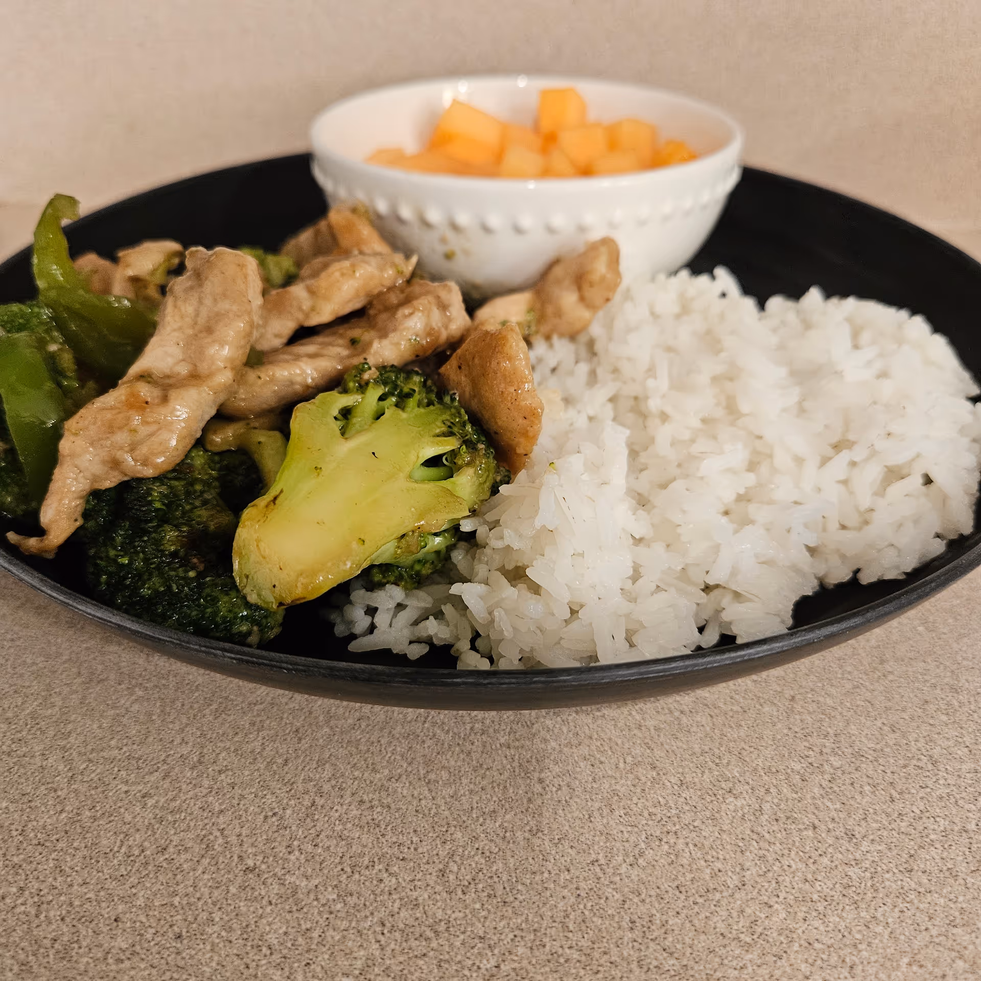 Plate of white rice with broccoli, sliced chicken, and diced fruit on a table.