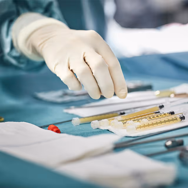 Close-up of gloved hand arranging syringes and surgical instruments on a sterile blue table.