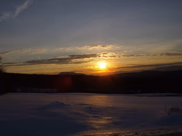Sunset over a snowy landscape with hills and a few clouds.