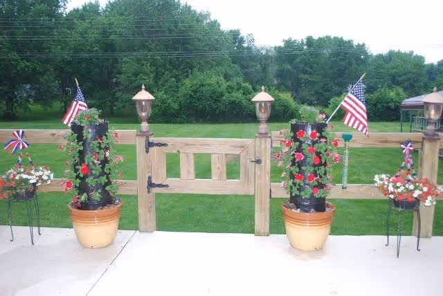 A wooden gate with potted flowers and American flags at Lovely Home ALF entrance.