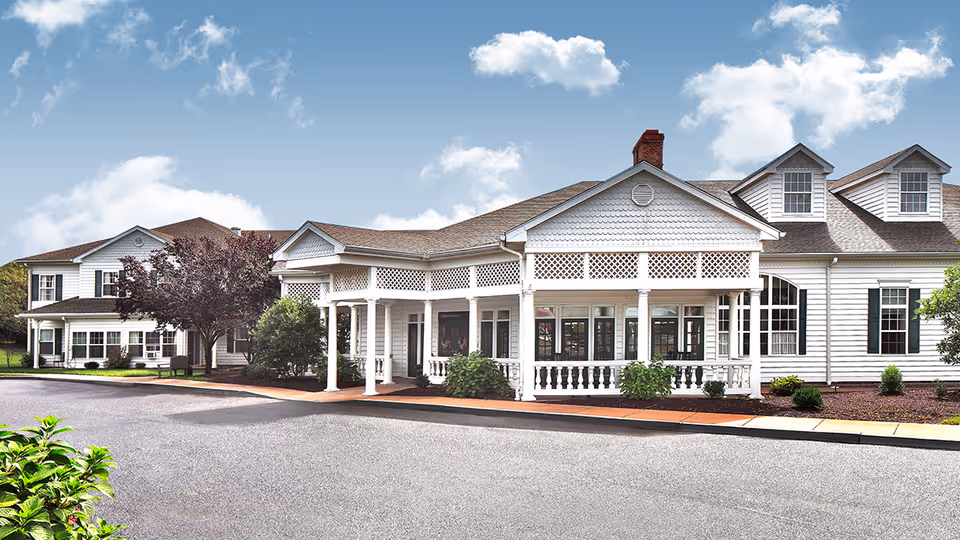 White senior living facility with a covered porch and landscaped exterior.