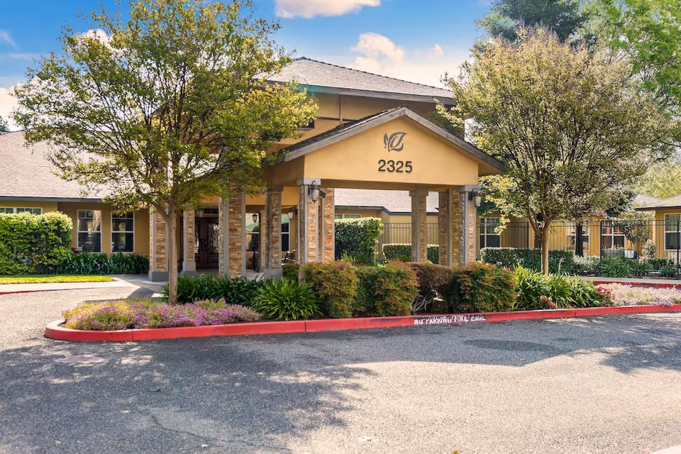 Front entrance of The Gardens of Modesto with a covered portico and surrounding landscaping.