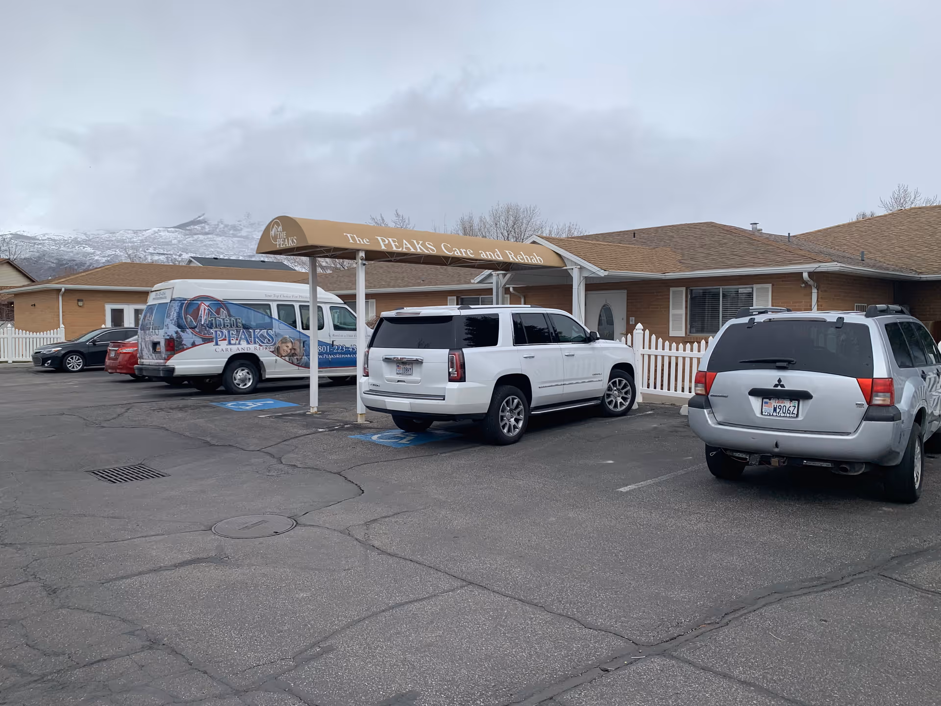 Exterior view of The Peaks Care and Rehab building with parked vans and a canopy.