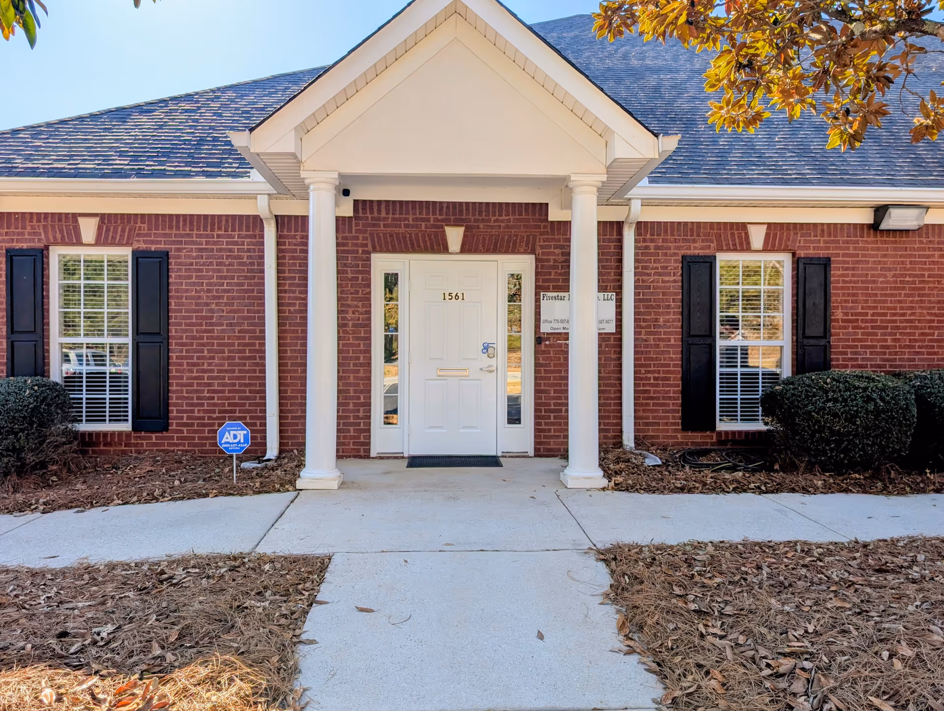 Brick senior living facility entrance with white columns, double doors, and a manicured walkway.