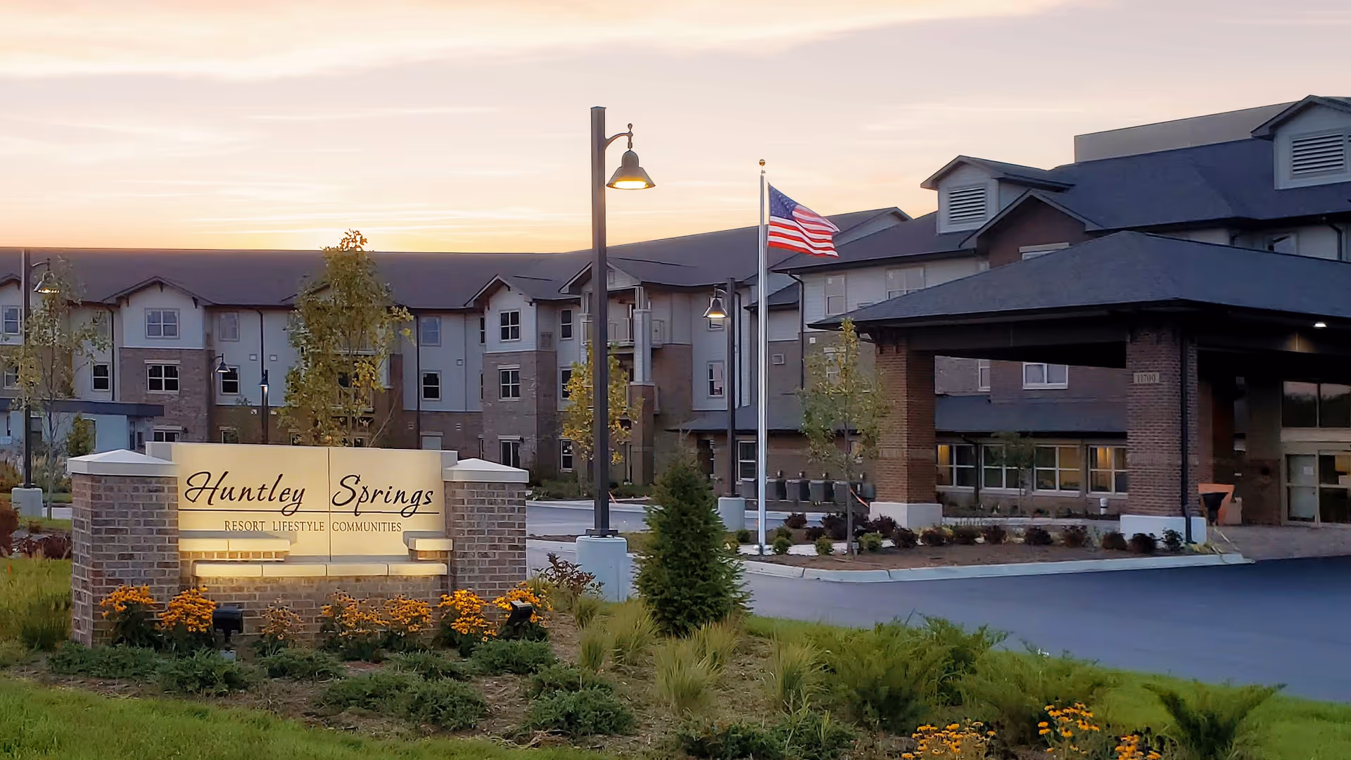 Exterior view of Huntley Springs Retirement Resort with sign, flag, and landscaped entrance.