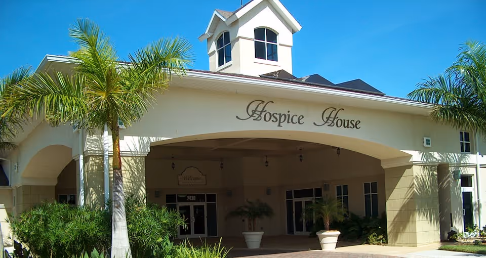 Front entrance of a beige hospice facility with palm trees and 'Hospice House' signage.