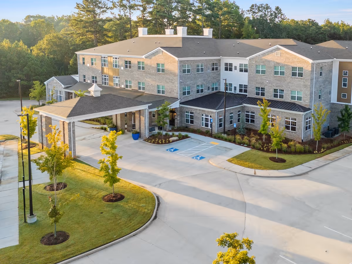 A modern, multi-story senior living facility exterior featuring a porte-cochere and landscaped grounds.