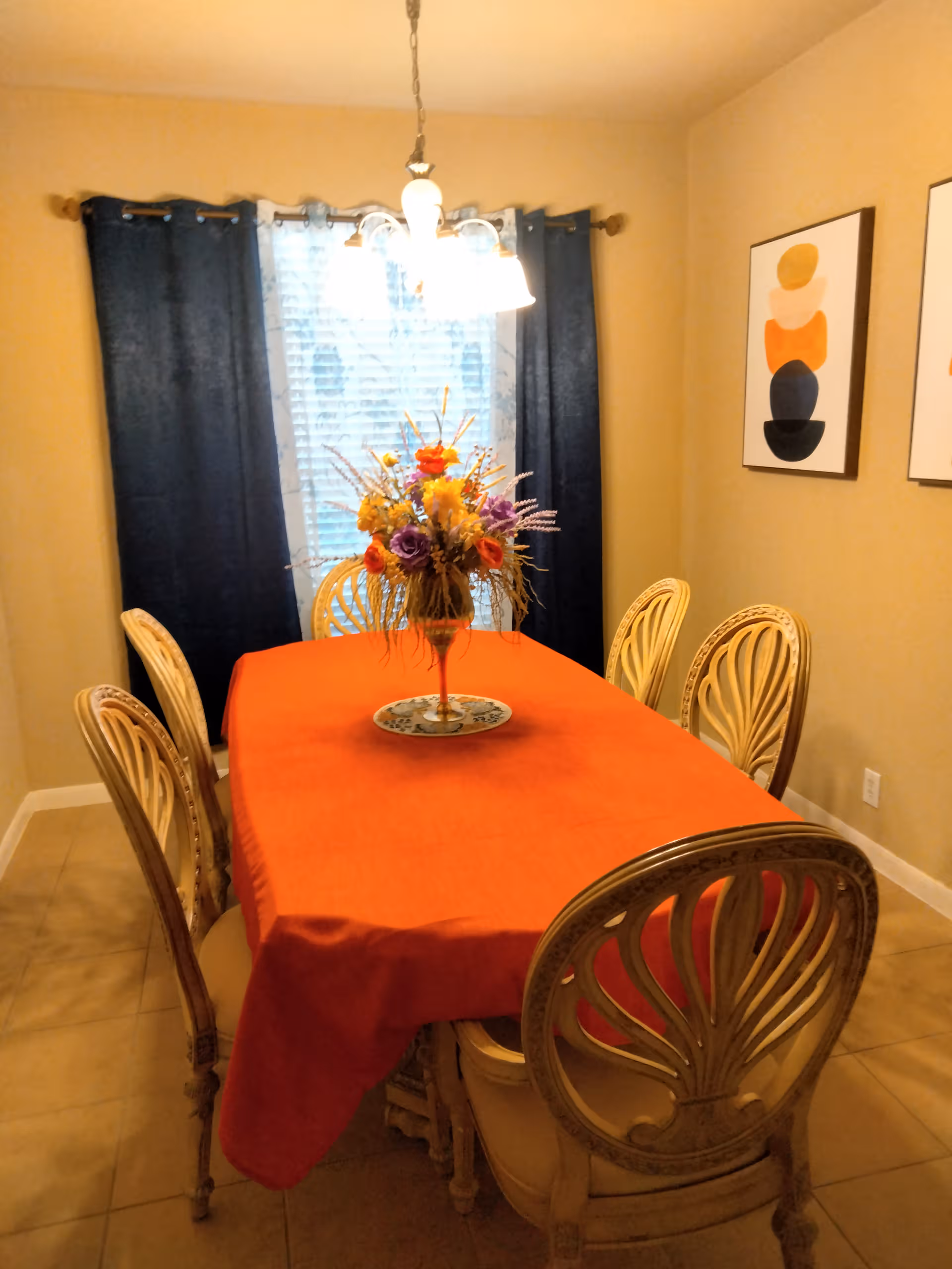Dining room with orange tablecloth, floral centerpiece, and wicker chairs.