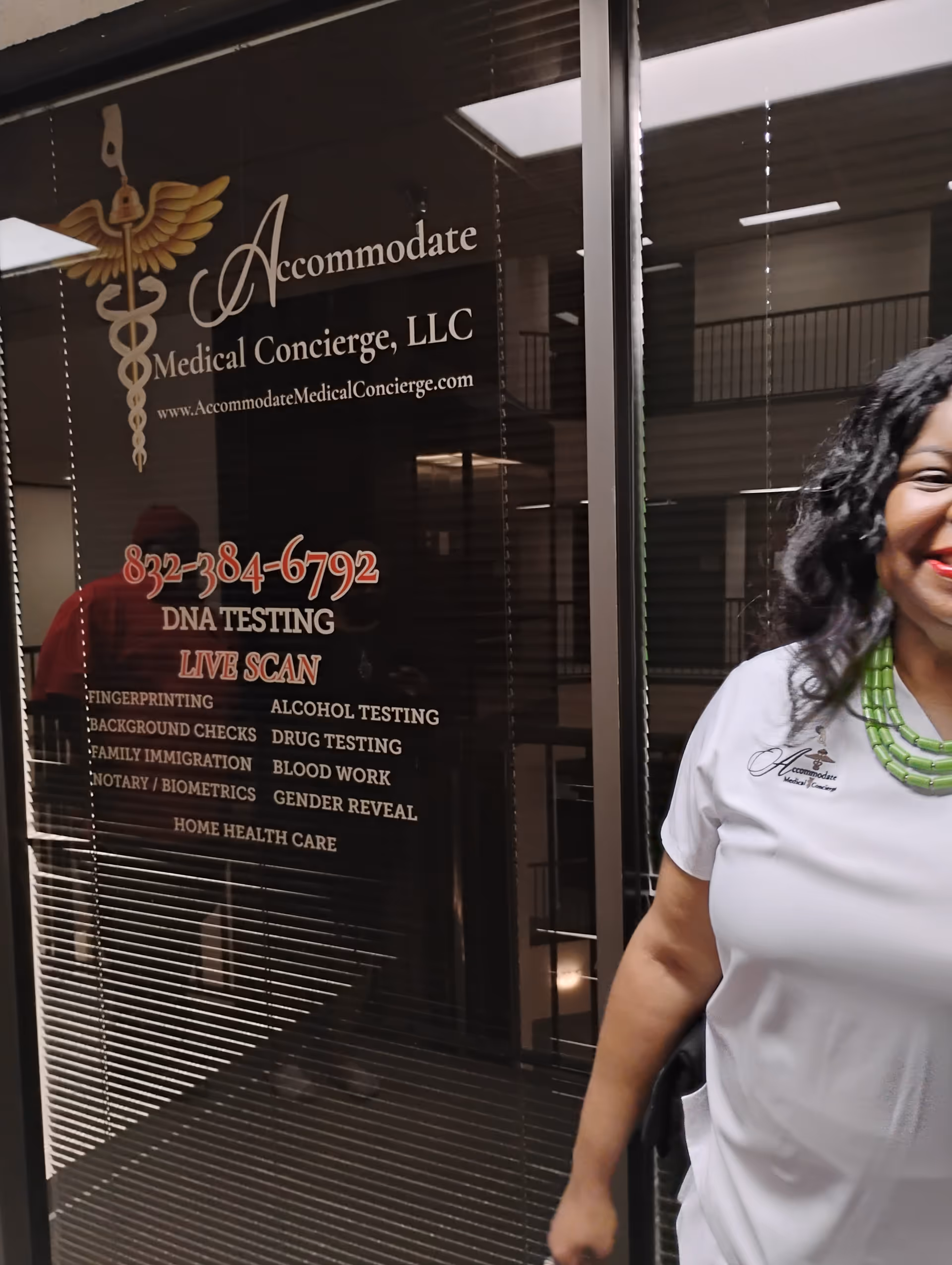 Smiling woman in white scrubs beside glass door displaying Accommodate Medical Concierge logo.