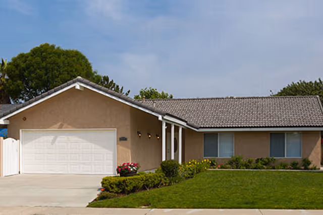 Front view of a single-story beige house with a two-car garage and manicured lawn