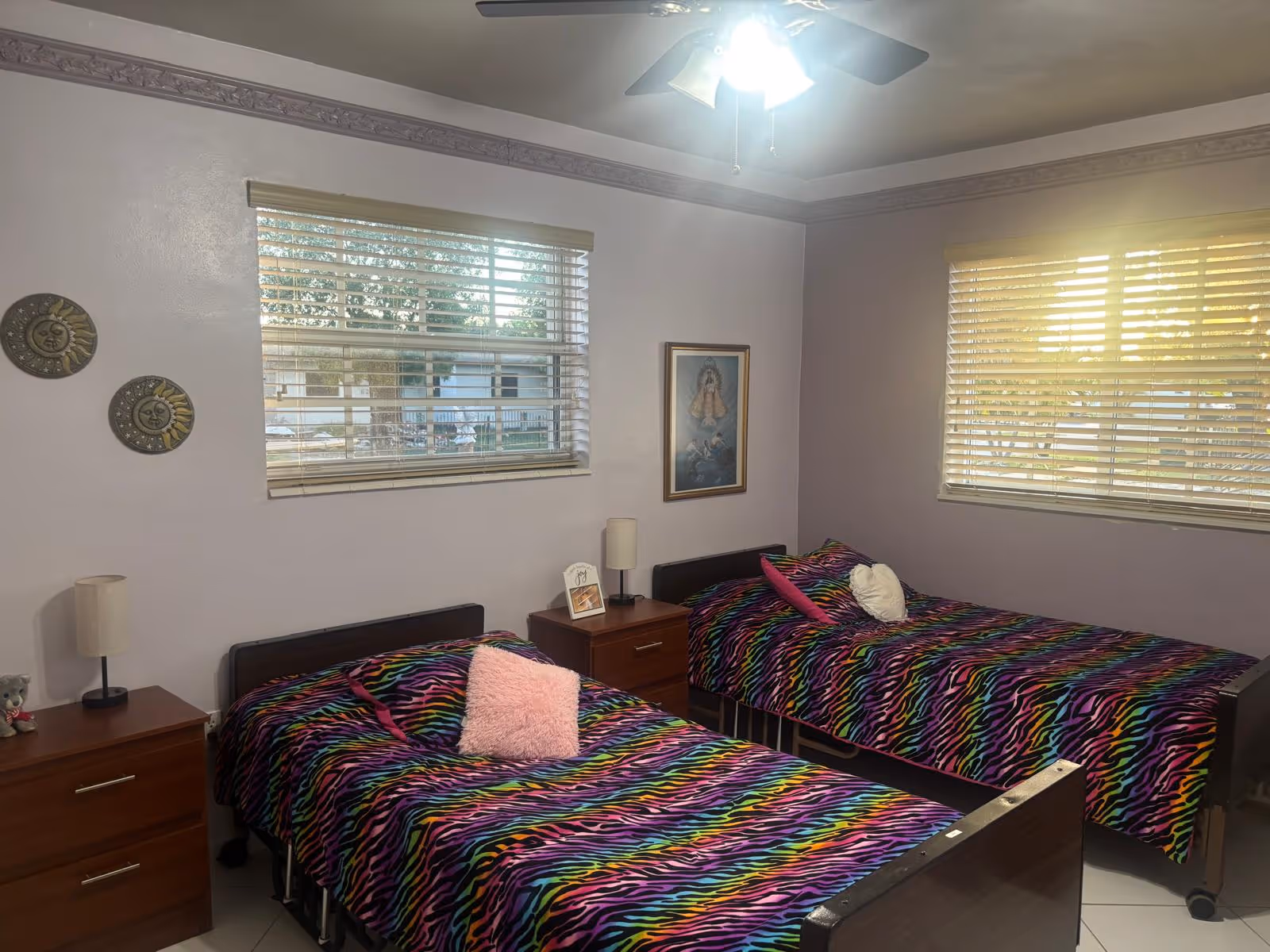 Two twin beds with zebra-print bedding, matching nightstands, and windows in a pastel-colored bedroom.