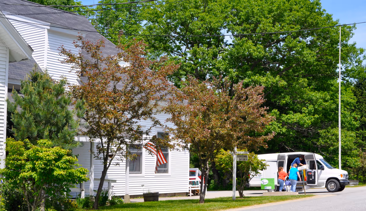 White Hodgdon Green senior living facility exterior with trees, a van, and people near the entrance.