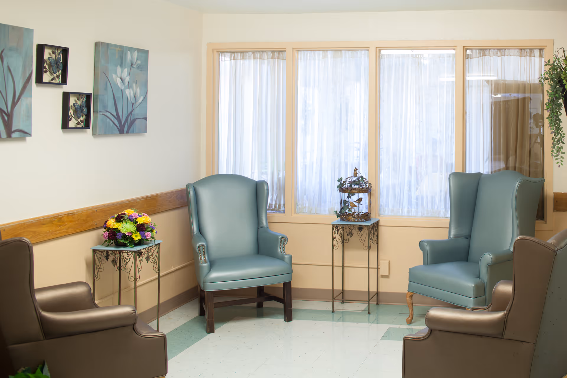 A softly lit seating area with four armchairs arranged around small side tables in front of large windows and wall art.