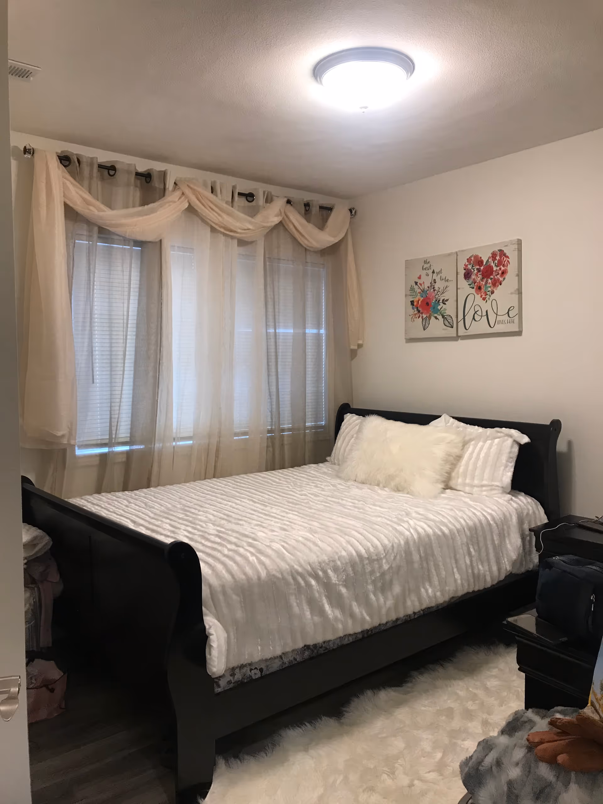 A neatly made bedroom with a large bed, sheer curtains, and wall art.