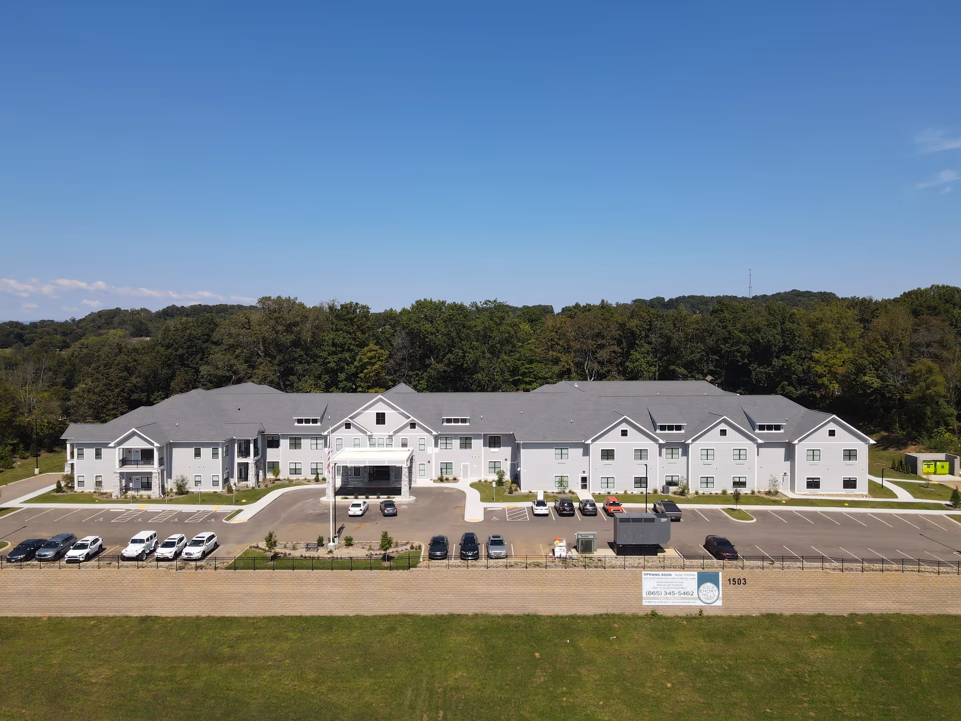 A large white senior living facility with a parking lot and surrounding trees.