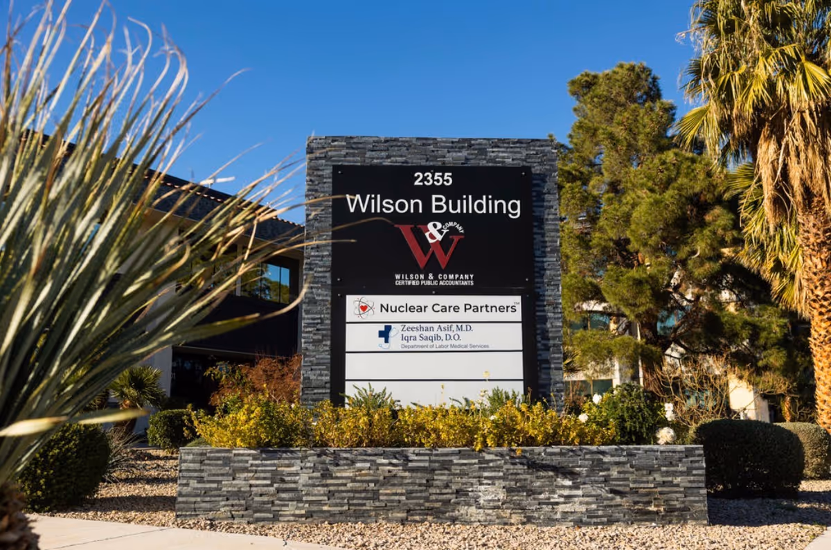 A stone building sign reads Wilson Building with Nuclear Care Partners amid desert landscaping.
