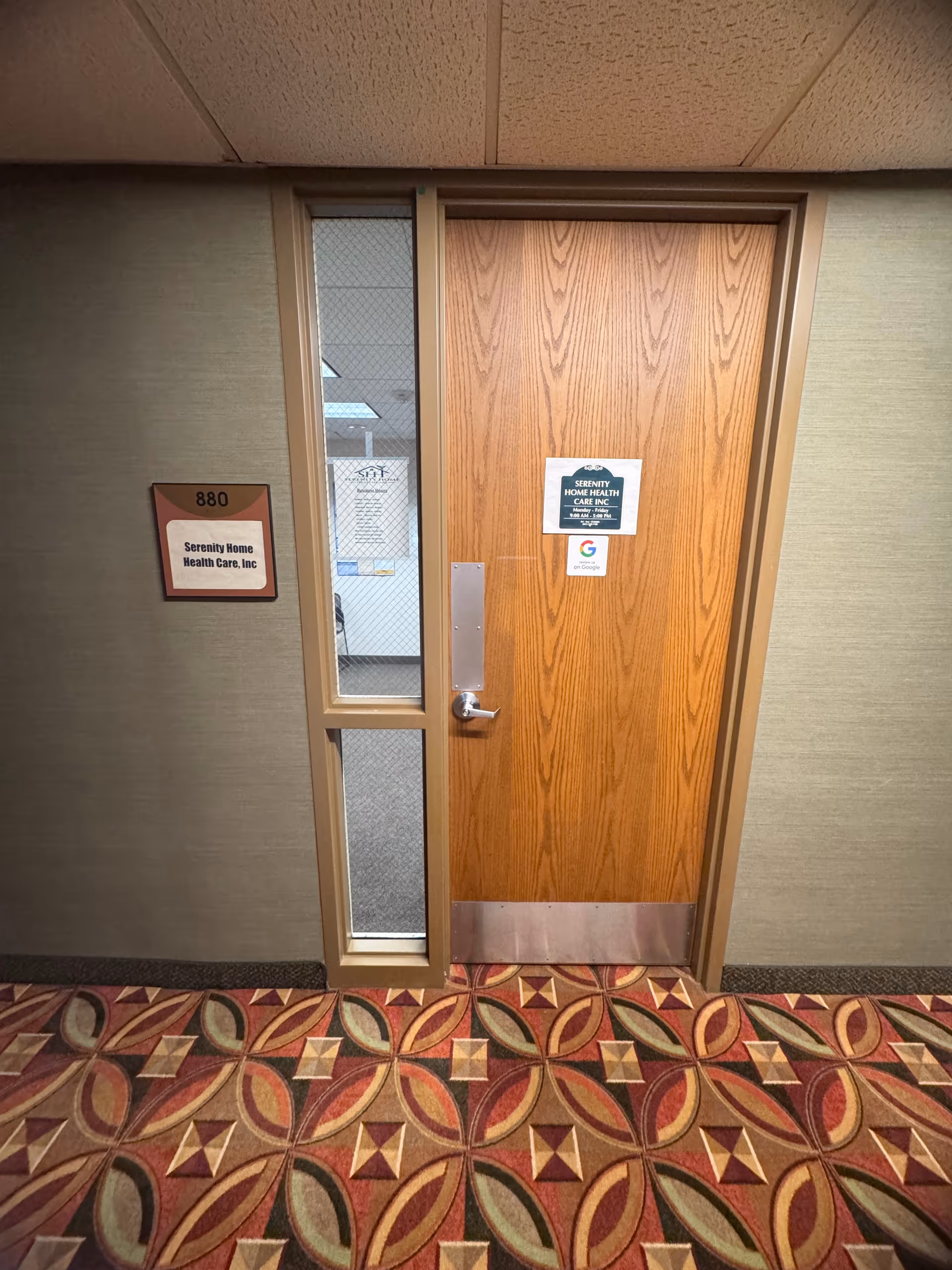 Interior hallway featuring wood door with glass panel, patterned carpet, and facility signage.