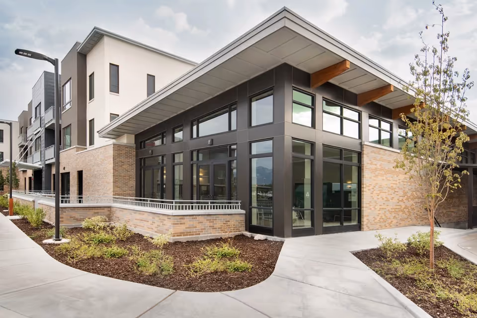 Modern senior living building exterior with large windows, brick and metal facade and landscaped walkways.