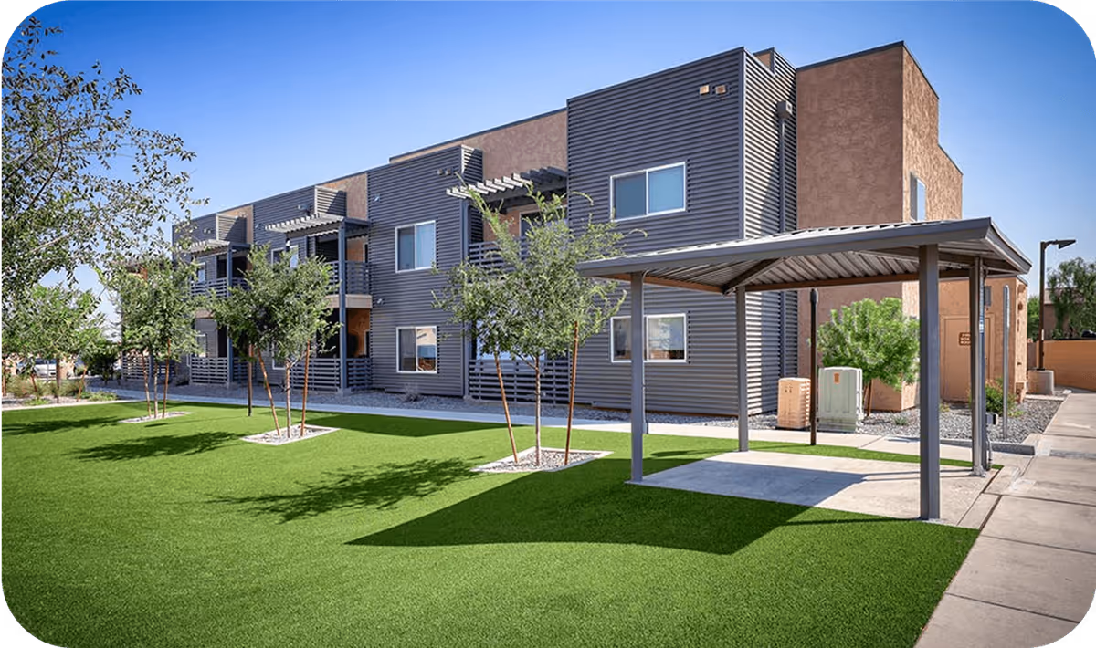 Exterior view of a modern senior living building with a green lawn, trees, and a covered walkway.