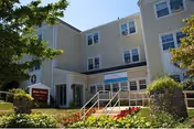 Front exterior of a beige senior living center with entrance stairs and landscaping.